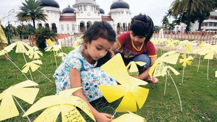 Blumen des Mitgefühls. Kinder stecken Papierblumen vor der Großen Baiturrahman-Moschee in Banda Aceh in Indonesien zum Gedenken in die Erde. Die Grüße kommen aus Japan, mehr als 40 000 Japaner haben eine handgeschriebene Nachricht mitgeschickt.