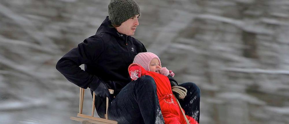 Ein Vater rodelt mit seinem Sohn den Berg herunter.
