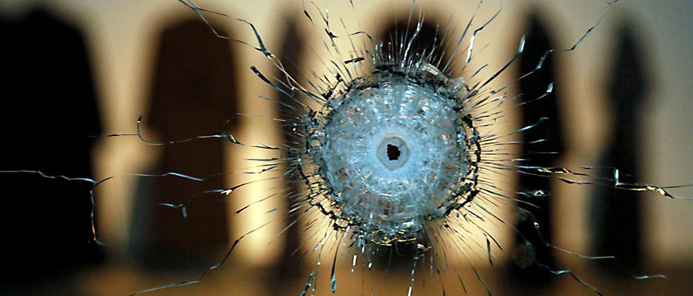 Glasbruch. Die Arbeit "A Hole" (2010), dahinter die sieben Mäntel von "Coats" mit Einschusslöchern.