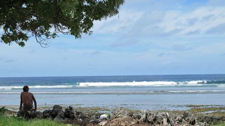 Ein Junge sitzt am Sandstrand auf der Fidschi-Insel Kiribati neben Abfällen.