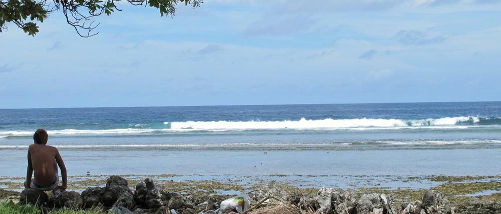 Ein Junge sitzt am Sandstrand auf der Fidschi-Insel Kiribati neben Abfällen.