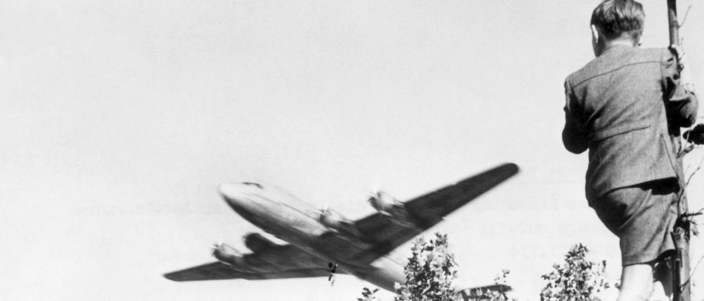 Archiv - Ein Junge verfolgt von einem Baum aus den Landeanflug eines US-amerikanischen Transportflugzeugs auf den Berliner Flughafen Tempelhof. Die Maschine bringt Versorgungsgüter nach West-Berlin. Als Reaktion auf die Währungsreform in den Westsektoren am 23.6.1948 verhängte die UdSSR am 24.6.1948 eine Blockade über Berlin. Alle Land- und Wasserwege wurden für den Personen- und Güterverkehr zwischen West-Berlin und Westdeutschland gesperrt. Die Versorgung der Westberliner Bevölkerung und der westalliierten Besatzung erfolgte daraufhin durch eine von den USA und Großbritannien errichtete Luftbrücke. Die Blockade wurde am 12. Mai 1949 aufgehoben. Foto: dpa (zu dpa «Vor 65 Jahren: Berlin gedenkt des Endes der Berliner Luftbrücke» vom 11.05.2014) +++(c) dpa - Bildfunk+++ | Verwendung weltweit