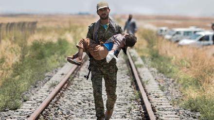 Ein kurdischer Kämpfer trägt ein verletztes Kind in Nordsyrien. Der Konflikt mit dem IS war einer der Gründe dafür, dass die Welt im vergangenen Jahr deutlich kriegerischer geworden ist.