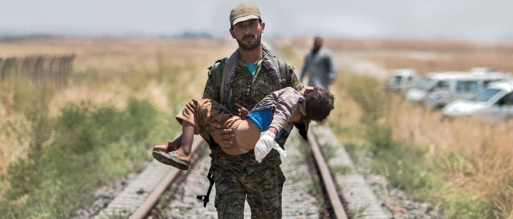 Ein kurdischer Kämpfer trägt ein verletztes Kind in Nordsyrien. Der Konflikt mit dem IS war einer der Gründe dafür, dass die Welt im vergangenen Jahr deutlich kriegerischer geworden ist. 