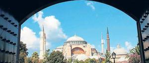 Menschen drängen sich auf einer Grünfläche, im Hintergrund ist eine große Moschee zu sehen.