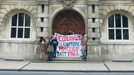 Denkmalsturz. „Dekolonialisiert die Bildung. Rhodes muss fallen“, fordern Studierende vor dem Oriel College in Oxford. Sie stören sich an der Statue des Südafrika-Kolonialisten Cecil Rhodes, die in der Nische unter dem Giebel steht. 