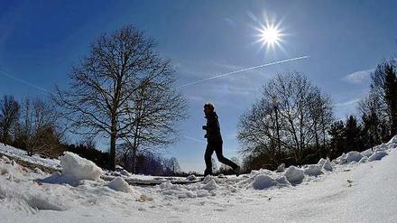 Jetzt auch im Sonnenschein. Ein Läufer joggt in Berlin durch den Schnee.
