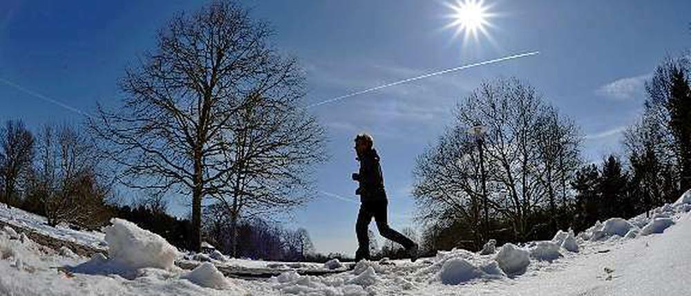 Jetzt auch im Sonnenschein. Ein Läufer joggt in Berlin durch den Schnee.