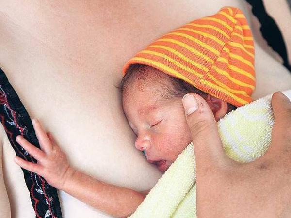 Eine Frau drückt ein Frühchen mit Ringelmütze an ihre Brust