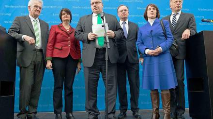 Erschöpft, aber doch erleichtert, haben Bundesumweltminister Peter Altmaier (CDU) in der Mitte des Bildes, die Ministerpräsidenten von Baden-Württemberg, Winfried Kretschmann (Grüne) ganz links im Bild, und von Niedersachsen, Stefan Weil (SPD), neben Altmaier im April den Endlagerkompromiss verkündet. Ganz rechts im Bild ist der grüne Fraktionsvorsitzende Jürgen Trittin zu sehen, neben ihm steht die FDP-Berichterstatterin Angelika Brunkhorst. Zwischen Kretschmann und Altmaier steht die Unions-Berichterstatterin Maria Flachsbarth (CDU). 