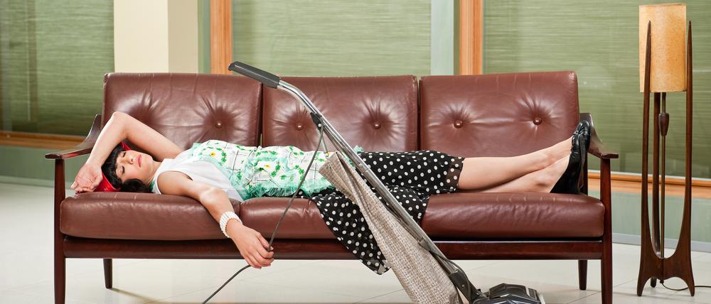 1950's housewife  with apron, napping on mid-sentury modern couch with Retro Hoover vacume cleaner