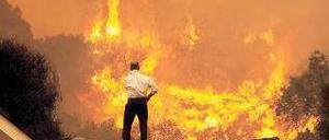 Bedrohlich. Ein Mann beobachtet von seinem Hausdach die Feuerwalze. Foto: AFP