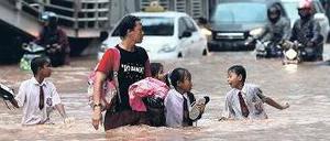 Schulkinder überqueren völlig durchnässt eine Straße im Banken- und Geschäftsviertel der Stadt. Sieben von zehn Bezirken sind überflutet.