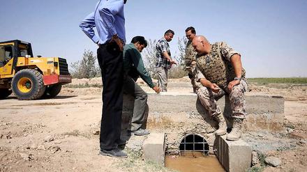 Bundeswehrsoldaten und Mitarbeiter einer Baufirma unterhalten sich in Masar-i-Scharif über ein Brückenbauprojekt.
