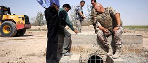 Bundeswehrsoldaten und Mitarbeiter einer Baufirma unterhalten sich in Masar-i-Scharif über ein Brückenbauprojekt.