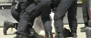 Das Video zeigt mehrere Beamte, die einen Mann in Handschellen am Boden halten. Der Beamte am linken Bildrand tritt darin mehrfach zu.