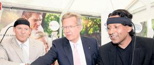 Am grünen Tisch des Sponsors. Ex-Bundespräsident Christian Wulff vergnügte sich 2011 beim Sommerfest im Schloss Bellevue am Stand des Mobilfunkunternehmens E-Plus mit Schauspieler Ralf Möller (l.) und Moderator Cherno Jobatey.