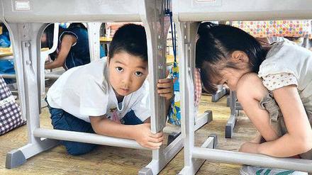 Unter den Tisch kriechen und die Tischbeine festhalten. Katastrophenübung in Tokio. 