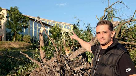 Ein Augenzeuge zeigt in Seiffen vor einem entwurzelten Baum auf das durch eine Windhose abgedeckte Dach des Erlebnisbads.
