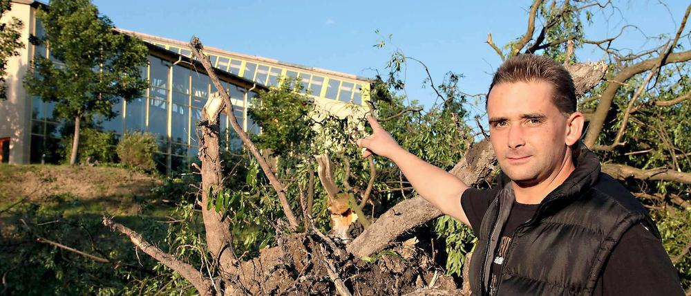Ein Augenzeuge zeigt in Seiffen vor einem entwurzelten Baum auf das durch eine Windhose abgedeckte Dach des Erlebnisbads.