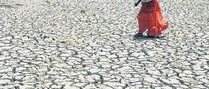 Eine Inderin überquert ein ausgetrocknetes Flussbett. Mikroversicherungen helfen auch bei Naturkatastrophen.