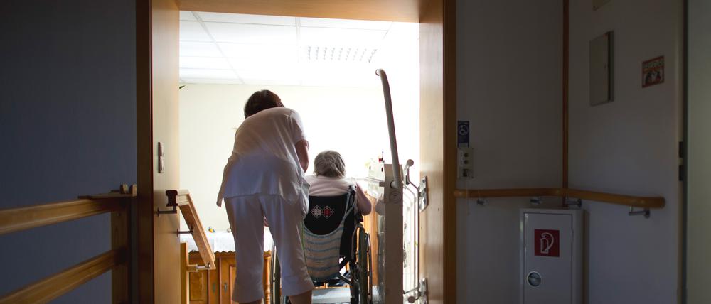 Eine Pflegerin hilft einer Bewohnerin eines Altenpflegeheimes mit einer Rollstuhlhilfe eine Treppe hinauf.