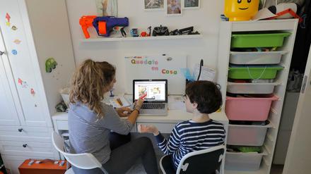 Eine Frau hilft ihrem Sohn vor einem Laptop bei den Hausaufgaben.