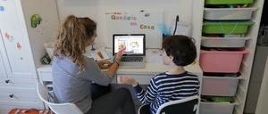 Eine Frau hilft ihrem Sohn vor einem Laptop bei den Hausaufgaben.