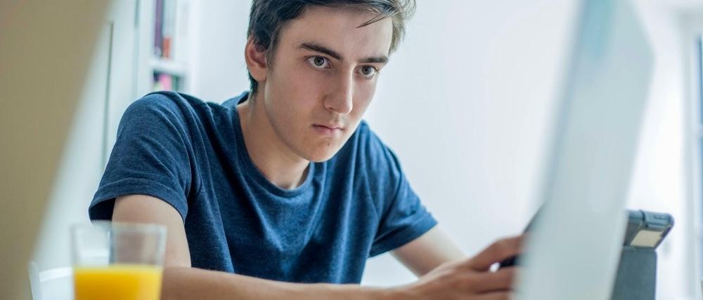 Ein Jugendlicher arbeitet an seinem Schreibtisch mit einem Laptop und einem Tablet.