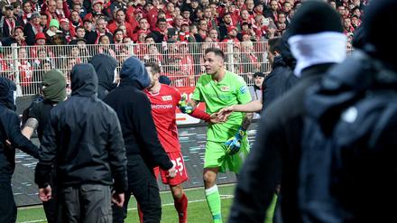 Unions Christopher Lenz und Rafal Gikiewicz beruhigen vermummte Fans ihres Vereins nachdem die Hertha-Fans Pyrotechnik auf das Spielfeld schießen.