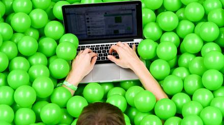 Eine Teilnehmerin der Internetkonferenz re:publica benutzt ihr Laptop in einem Bällebad mit grünen Bällen. 