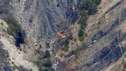 Ein Helikopter fliegt über eine Stelle, an der Helfer neben Wrackteilen arbeiten.