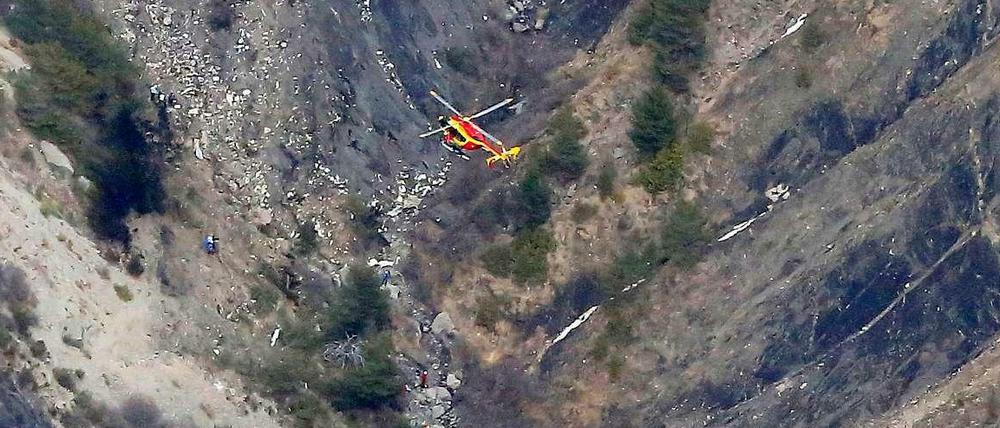 Ein Helikopter fliegt über eine Stelle, an der Helfer neben Wrackteilen arbeiten.