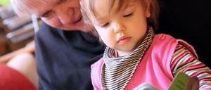 Eine ältere Frau liest einem Kleinkind aus einem Buch vor.