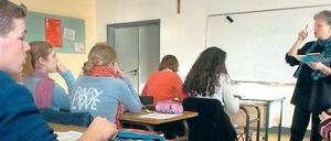 Schüler und Schülerinnen sitzen im Klassenraum, vor ihnen steht eine Lehrerin.