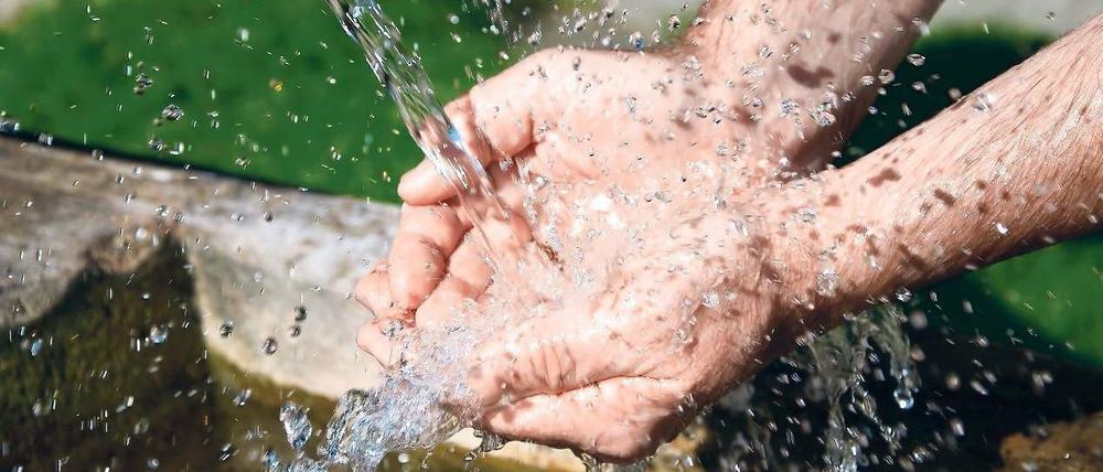 Eine Person fängt mit beiden Händen Wasser auf, das aus einer Quelle sprudelt.