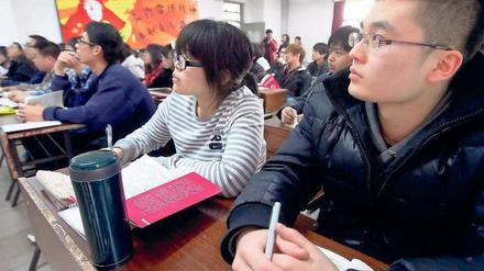 In einer Universität in Peking sitzen Studierende im Seminarraum, im Hintergrund ein Wandbild von Lei Feng, Soldat der chinesischen Volksbefreiungsarmee.