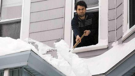 Ein Mann in Boston schaufelt Schnee von seinem Vordach. Er hat sich mit den Schneebergen noch nicht so angefreundet, wie es scheint. Warum springt er nicht aus dem Fenster, wie es viele seiner Nachbarn unternehmen?
