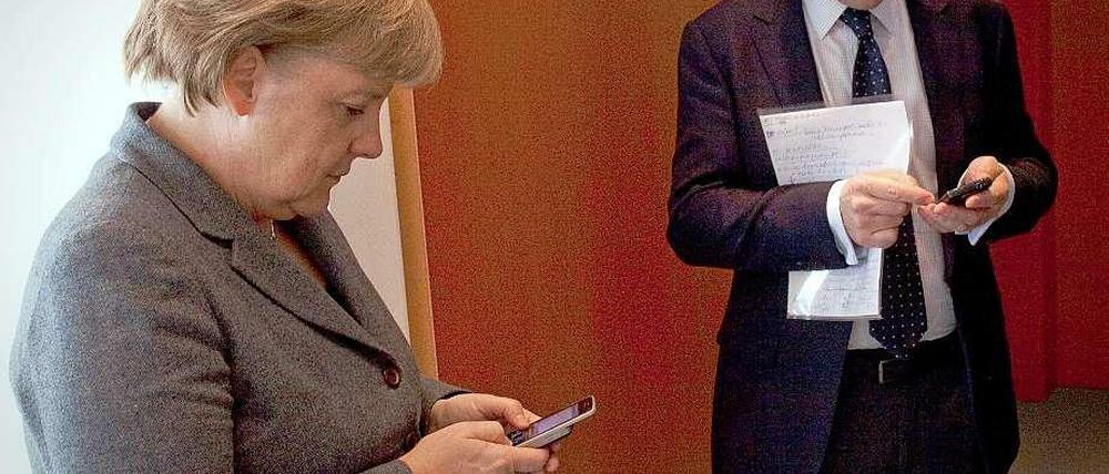 Bundeskanzlerin Angela Merkel und Regierungssprecher Steffen Seibert mit ihren Smartphones.