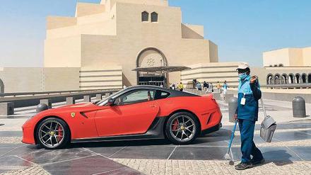 Reichtum und Ausbeutung. Ein ausländischer Arbeiter steht vor einem Ferrari in Katar.