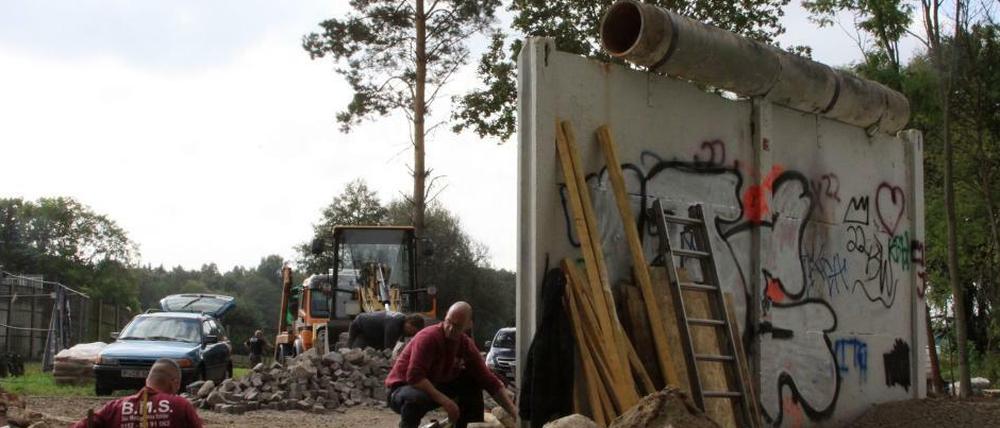 Was von der Berliner Mauer noch steht. Arbeiter sanieren das Stück; links hinter dem Zaun befindet sich Berlin-Spandau, der Ortsteil Kladow.