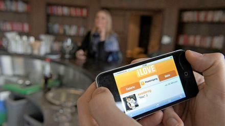 Ein Mann nutzt in einer Bar auf seinem iPhone das Flirtportal iLove. Die mobile Webseite erlaubt das Flirten unterwegs und überall.
