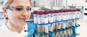 Eine Labormitabeiterin trägt ein Gestell mit Reagenzgläsern durch den Raum.