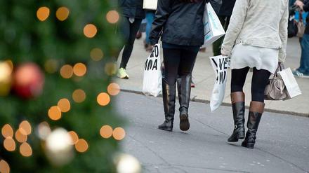 Zwei Frauen gehen mit dünnen Einkaufstüten an einem geschmückten Tannenbaum vorbei.
