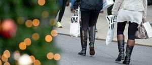 Zwei Frauen gehen mit dünnen Einkaufstüten an einem geschmückten Tannenbaum vorbei.