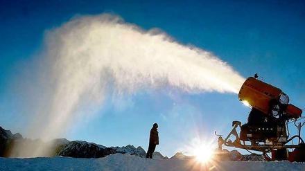 Eine Schneekanone schießt in hohem Bogen Schnee in den blauen Himmel. 