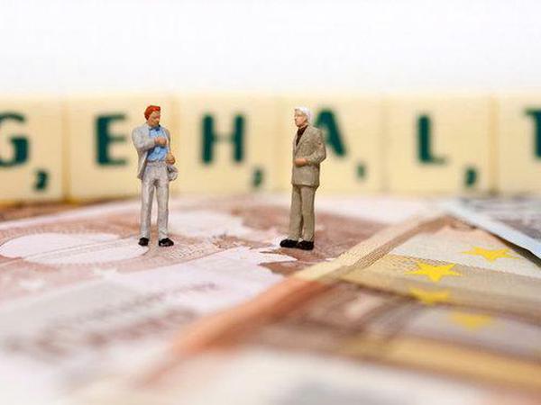 Brutto-Netto-Rechner: Zwei Männer stehen auf Geldscheinen, hinter ihnen steht das Wort Gehalt auf Scrabble-Buchstaben
