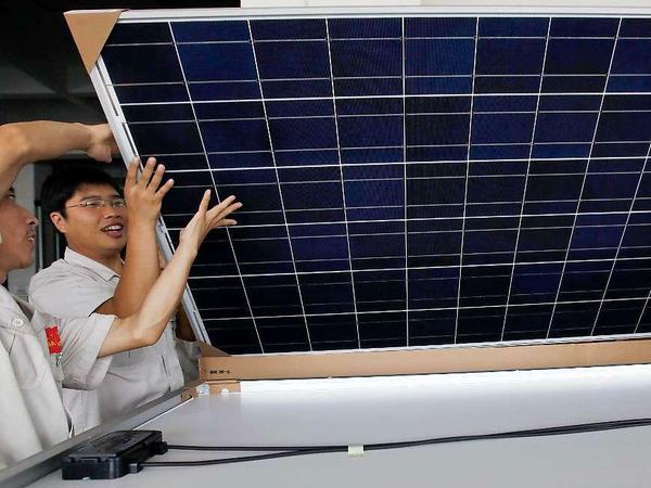Chinesische Arbeiter verpacken ein großes viereckiges Solarpanel.