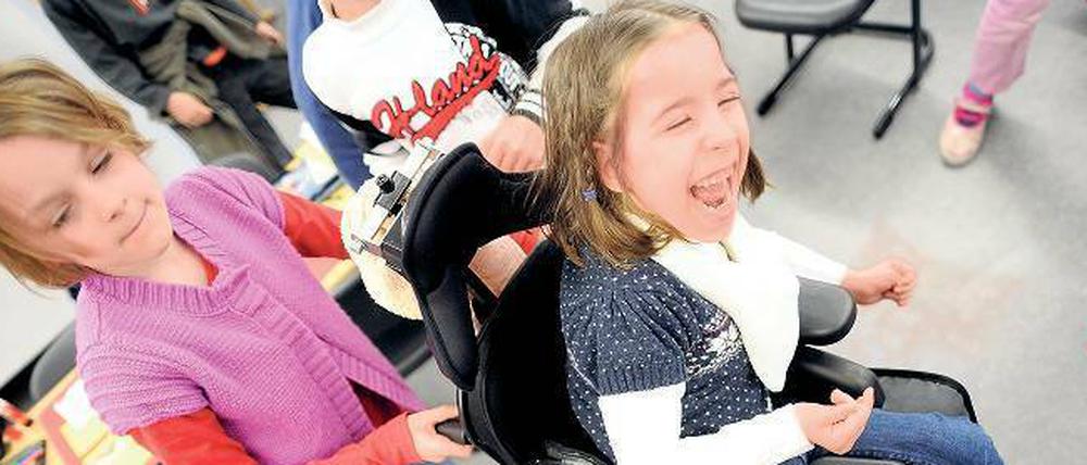 Ein Mädchen schiebt ein anderes Mädchen im Rollstuhl.