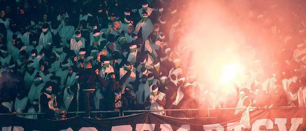 Geisterspiel. Weiß vermummt zündeln Chaoten im Block von Hannover 96 und schmähen Eintracht Braunschweig mit Plakaten.  Foto: dpa